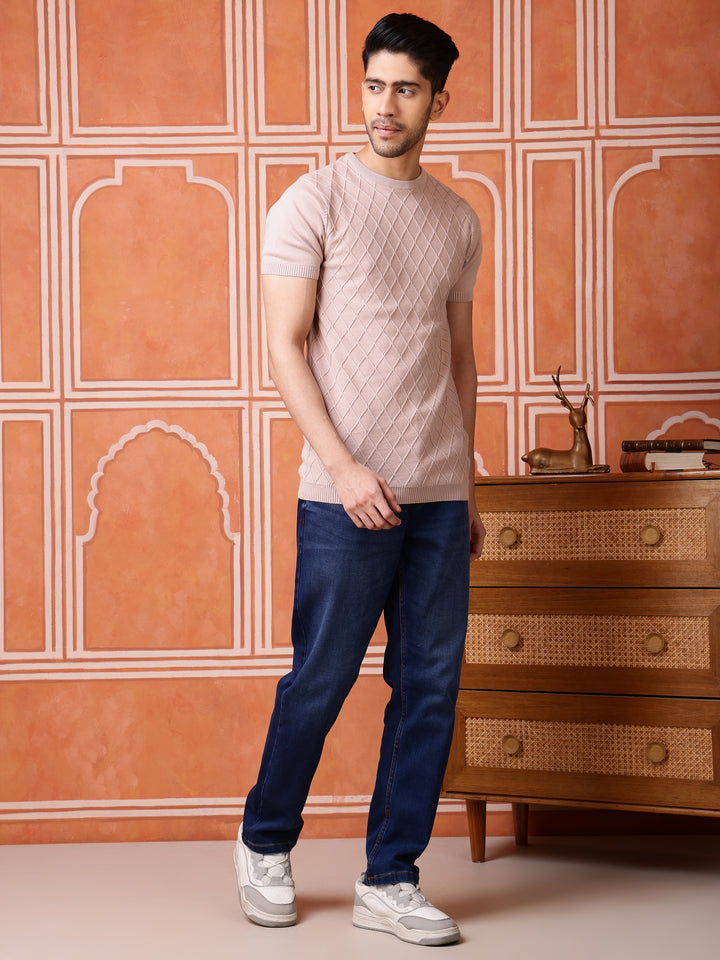 Man wearing a patterned shirt and jeans standing in front of an ornate wall and wooden dresser.